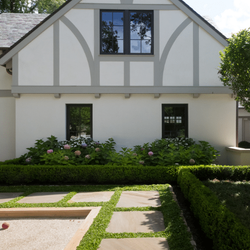 Paved walkway edged with shrubbery with hydrangeas under windows of house